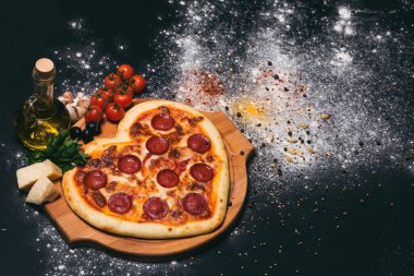 Pepperoni, domates, mozzarella, sarımsak ve siyah arka planda maydanoz şeklinde pizza kalbi.