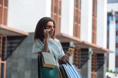 Kredi kartı tutan ve online alışveriş için cep telefonu kullanan bir kadın.