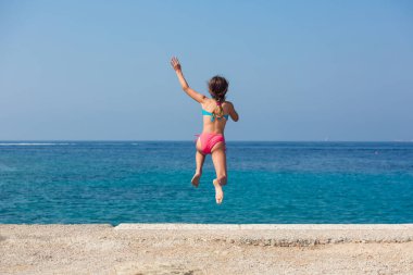 Küçük kız bir iskeleden denize atlıyor.