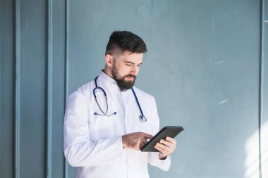 Sağlık hizmeti, tıp konsepti: Sakallı yakışıklı doktor tablet bilgisayarında tanı koymayı düşünüyor