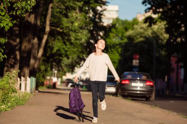 Çocuk güneşli bir günde okul çantasıyla koşuyor.