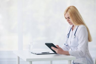Kafkasyalı kadın doktor tablet kullanıyor ve tıbbi belgelerle teşhis koyuyor.