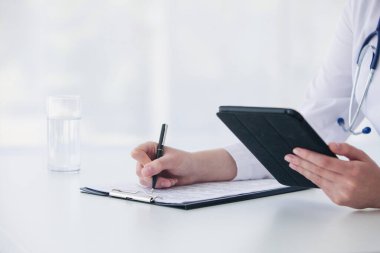 Kafkasyalı kadın doktor tablet kullanıyor ve tıbbi belgelerle teşhis koyuyor.