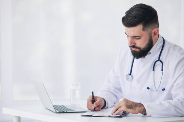 Doktor, tıbbi ofisinde belge ve dizüstü bilgisayarla çalışıyor.