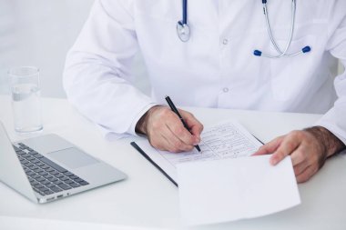 Doktor, tıbbi ofisinde belge ve dizüstü bilgisayarla çalışıyor.