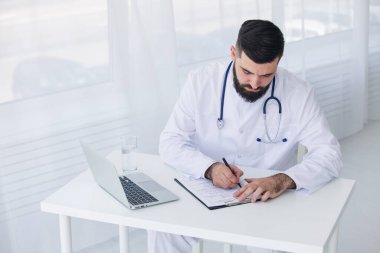 Doktor, tıbbi ofisinde belge ve dizüstü bilgisayarla çalışıyor.