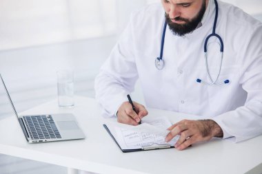 Doktor, tıbbi ofisinde belge ve dizüstü bilgisayarla çalışıyor.