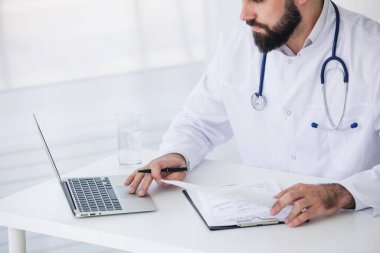 Doktor, tıbbi ofisinde belge ve dizüstü bilgisayarla çalışıyor.