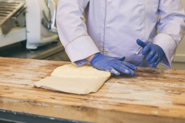 Şef ahşap kesme tahtasında kruvasan pişirmek için hamur katlıyor.