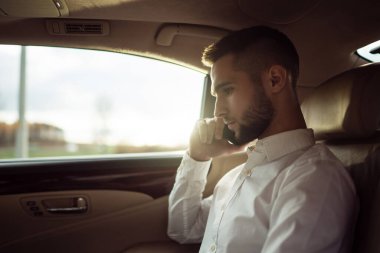 Akıllı telefondan konuşan adam arabanın arka koltuğunda oturuyor, iş adamı takside.
