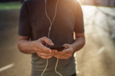 Gün batımında akıllı telefon ve kulaklıkla stadyumda yetmiş yaşında bir koşucu. Akşam koşusu