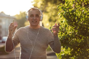 Kıdemli adam kaldırımda yürüyor müzik dinliyor ve şarkı söylüyor.