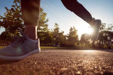 Koşan ayaklar yolda, ayakkabıya yakın gidiyor. Gün batımında parkta koşan genç bir sporcu