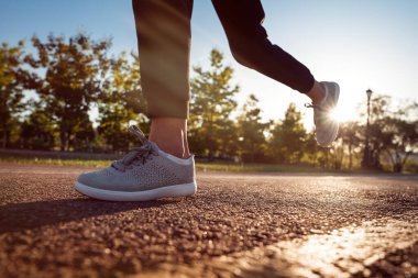 Koşan ayaklar yolda, ayakkabıya yakın gidiyor. Gün batımında parkta koşan genç bir sporcu