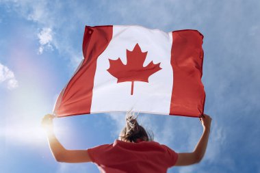 Child girl is waving Canadian flag on top of mountain at sky background clipart