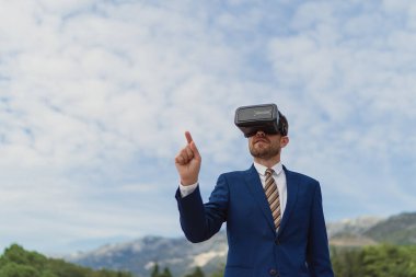 İş adamı gökyüzünün arka planında sanal bir gerçekliği görüntülemek için VR-kulaklık kullanır