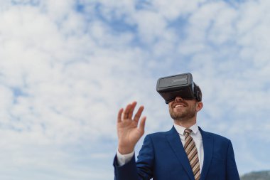 İş adamı gökyüzünün arka planında sanal bir gerçekliği görüntülemek için VR-kulaklık kullanır