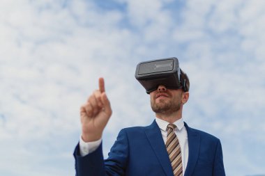 İş adamı gökyüzünün arka planında sanal bir gerçekliği görüntülemek için VR-kulaklık kullanır
