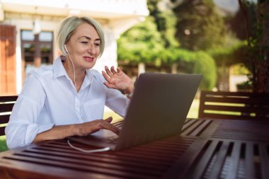 Kafede dinlenirken bilgisayarla görüntülü konuşma yapan mutlu olgun bir kadın.