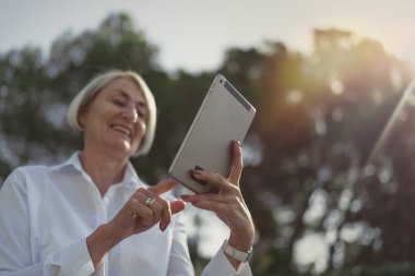 Parkta dinlenirken tablet kullanan olgun bir kadın.