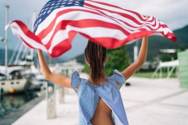 Çocuk Amerikan bayrağını deniz ve yatların arkasında sallıyor.