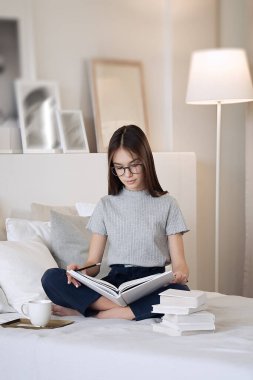                                Evde kitap okuyup ödevlerini yapan tatlı bir genç kız. Eğitim, çocuklar ve okul konsepti, uzaklık eğitimi, öz eğitim  