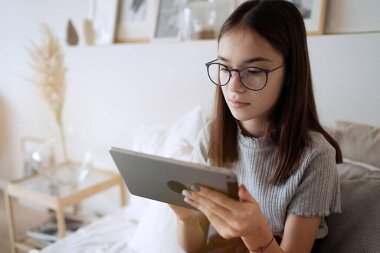                               Evde yatakta tablet kullanan tatlı bir genç kız. Gözlük takan genç ve güzel bir kız. İnternette okuyor, uzaktan öğreniyor, kendini eğitiyor.