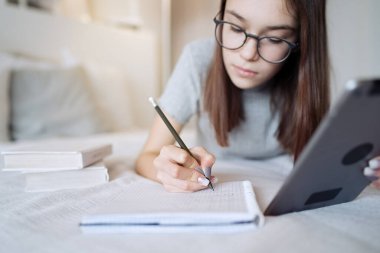                                Evde yatakta tablet kullanan tatlı bir genç kız. Gözlük takan genç ve güzel bir kız. İnternette okuyor, uzaktan öğreniyor, kendini eğitiyor.