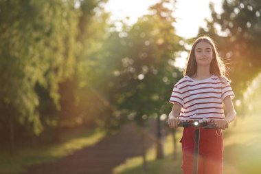                                Gün batımında parkta elektrikli scooter kullanan tatlı bir genç kız.     