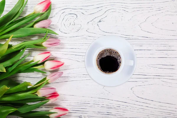 Cup of coffee near tulips on wooden background