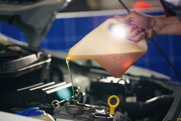 Auto mechanic is changing motor oil into a engine at car station