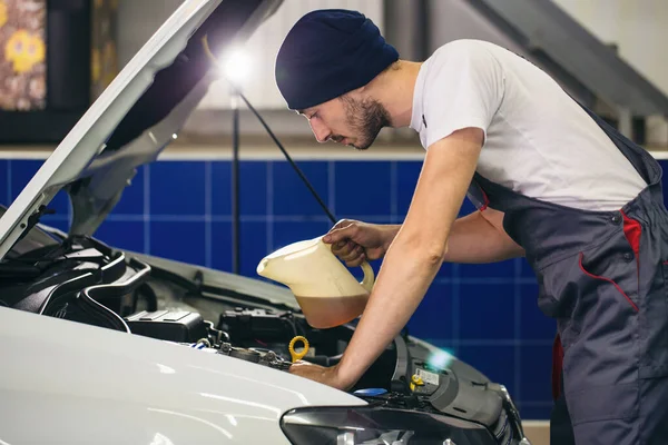 Auto mechanic is changing motor oil into a engine at car station