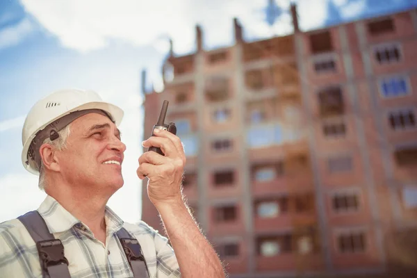 Senior engineer builder using a walkie talkie at a construction site. Sunset time