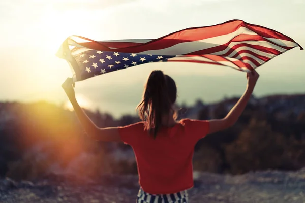 子供の女の子は空の背景で山の上にアメリカ国旗を振っている 日没時間 — ストック写真