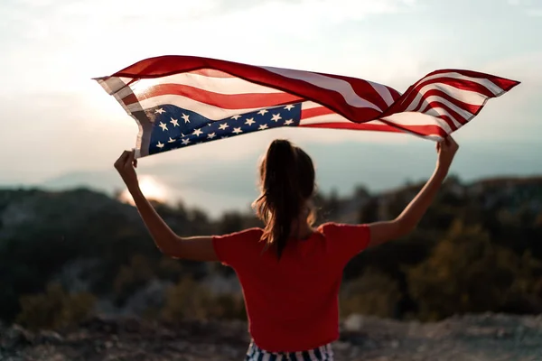 Çocuk kız, arka planda dağın tepesinde Amerikan bayrağı sallıyor. Gün batımı zamanı