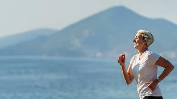 Sunrise 'da yaşlı bir kadın koşuyor. Sabah arka planda, deniz ve dağlarda koşarken