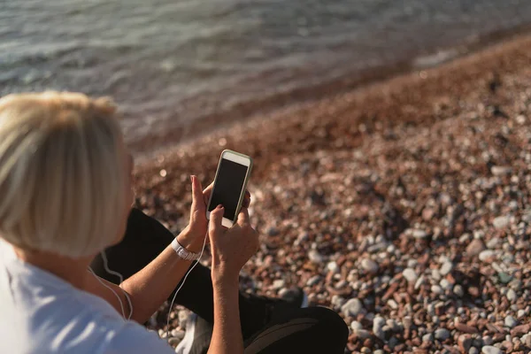 Dojrzała Kobieta Siedzi Joggingu Plaży Starsza Pani Używająca Smartfona Słuchawek — Zdjęcie stockowe
