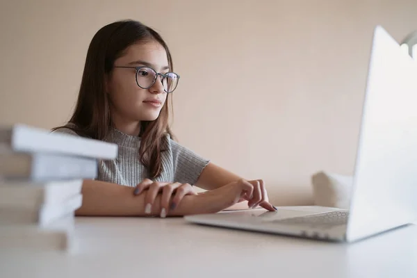                            Güzel genç kız evde masanın arkasında oturmuş ödev yapıyor. Gözlüklü güzel bir kız, internetten bilgisayarla öğreniyor, uzaktan öğreniyor, kendini eğitiyor.    