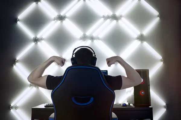 Back view of young gamer guy in headphones screaming and rejoicing unleash power while playing video games on computer young man shows his biceps