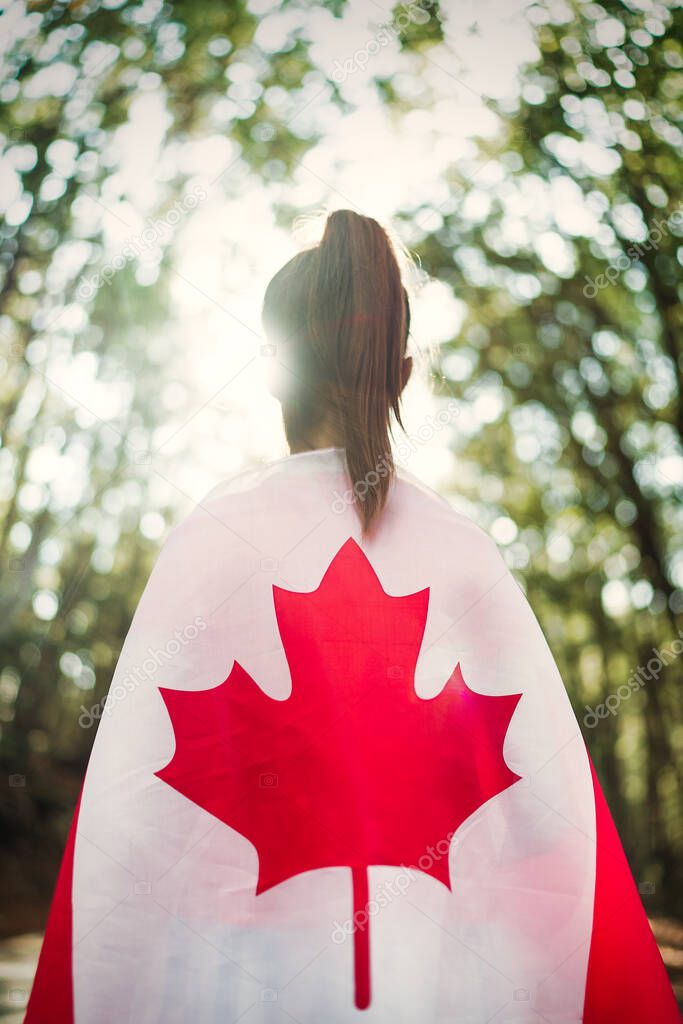 Child teenager girl at nature background an Canada flag on her shoulders  