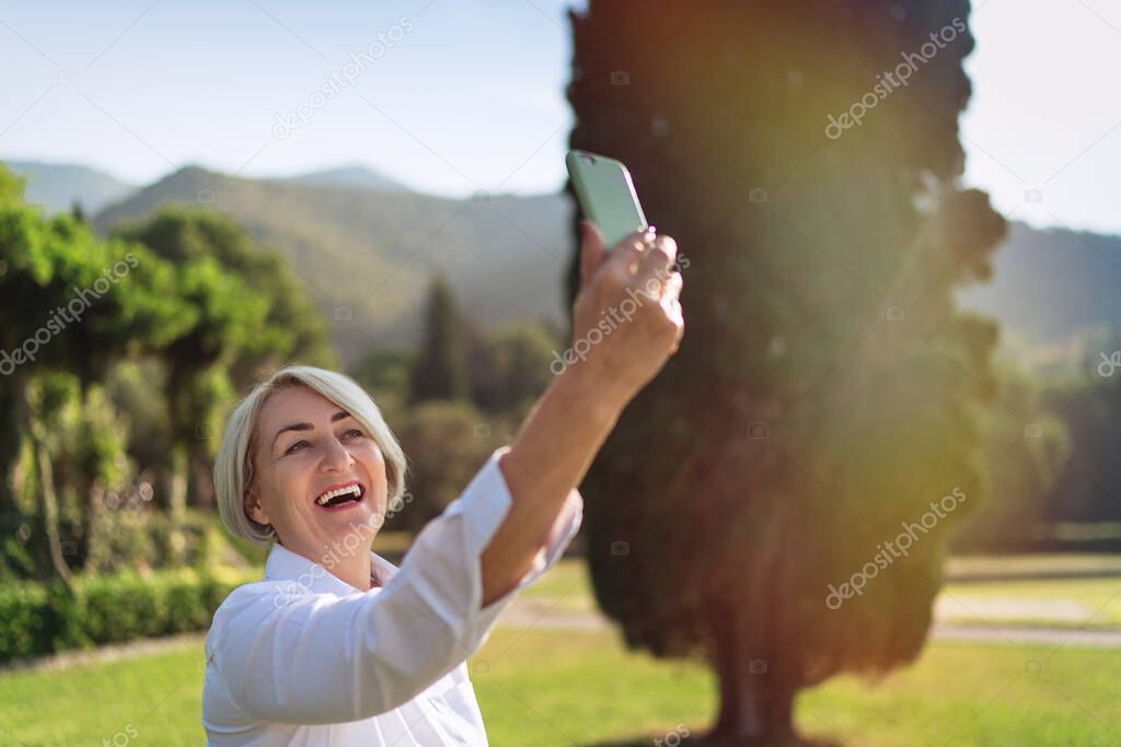 Senior woman taking a selfie with mobile phone while resting at the park 