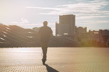                                Son sınıf öğrencisi gün batımında şehirde elektrikli scooter kullanıyor.  
