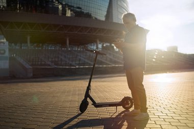                                Son sınıf öğrencisi elektrikli scooterla gezdikten sonra akıllı telefon kullanıyor.     