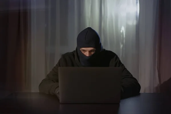 Male hacker in the hood in a dark room using computer virus program for cyber attack. Hackers and cyber security concept