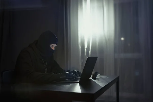 Male hacker in the hood in a dark room using computer virus program for cyber attack. Hackers and cyber security concept