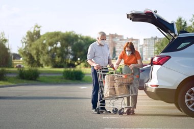                                Maskeli yaşlı çift süpermarketin önünde arabaya alışveriş yapıyor.       