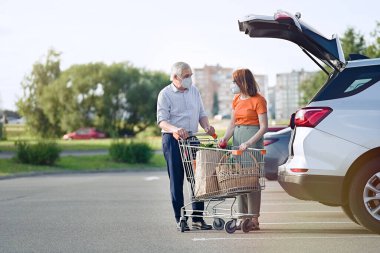                                Maskeli yaşlı çift süpermarketin önünde arabaya alışveriş yapıyor.       