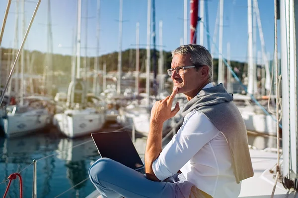 Senior businessman is working during the vacation on a sailboat