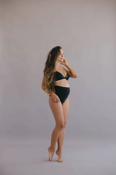 Pregnant woman with long curly hair in black underwear.