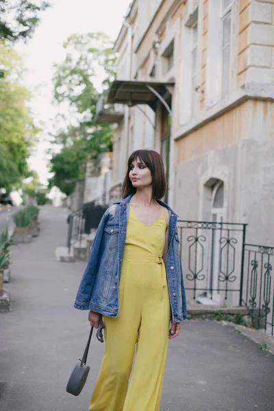 Woman in stylish yellow jumpsuit posing on city streets.